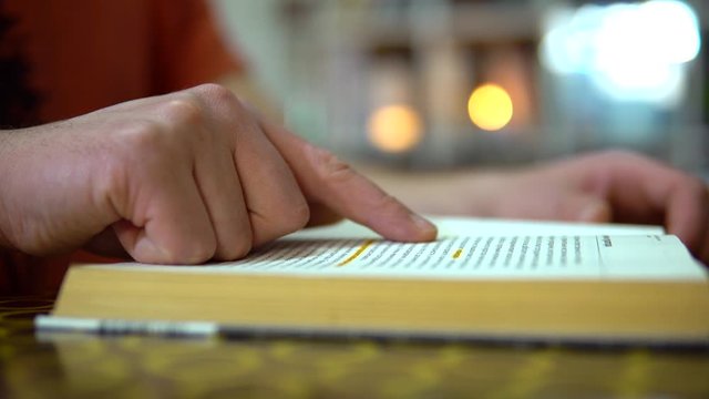 Quick read. A finger moves along the lines of a book. The guy turns the pages of the book.