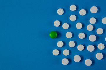many white pills and one green on a blue background