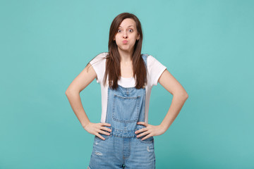 Fototapeta premium Pretty young brunette woman girl in casual denim clothes posing isolated on blue turquoise background. People lifestyle concept. Mock up copy space. Standing with arms akimbo on waist, blowing cheeks.