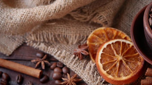 Still life.Coffee beans in a clay cup, cinnamon sticks, dried oranges, pieces of sugar on a background of burlap. Camera movement left to right. 4k video