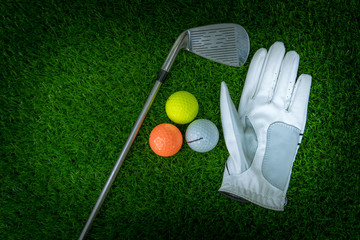 A golf glove ,colorful ball ,tee and gold club put on green grass of golf course ,This objects for play