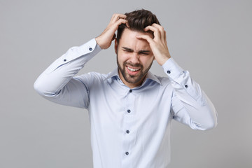 Sick exhausted young unshaven business man in light shirt posing isolated on grey wall background. Achievement career wealth business concept. Mock up copy space. Put hands on head, having headache.