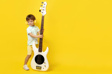 Full lengh photo of charming kid play white electric bass guitar over yellow background.