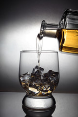 pours rum from a decanter into an ice glass