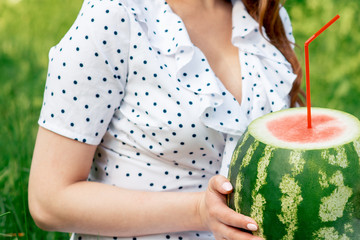 Girl holds whole watermelon with cocktail straw on green summer background.