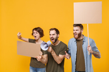 Angry protesting young people hold protest signs broadsheet blank placard on stick scream in megaphone point aside isolated on yellow background. Protests strikes picket concept. Youth against city.