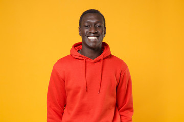 Smiling young african american man guy in red streetwear hoodie posing isolated on yellow background studio portrait. People sincere emotions, lifestyle concept. Mock up copy space. Looking camera.