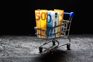 shopping cart with a blue handle with euro bills on black concrete dark background .copy space