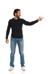 Handsome Man Is In Black Blouse And Jeans Is Looking Away And Pointing At The Side.