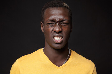 Obraz premium Close up of displeased disgusted young african american man guy in yellow t-shirt posing isolated on black background studio portrait. People lifestyle concept. Mock up copy space. Looking camera.