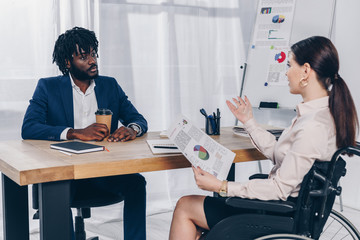 African american recruiter and disabled employee on wheelchair talking at table in office