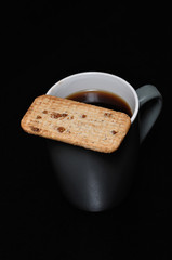 A mug of black coffee with a biscuit on top