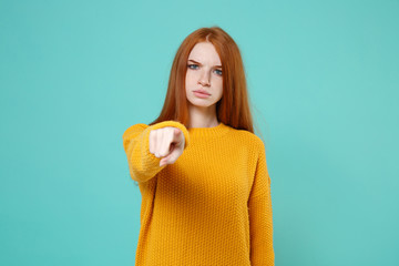 Strict displeased young redhead woman girl in yellow sweater posing isolated on blue turquoise wall background in studio. People lifestyle concept. Mock up copy space. Pointing index finger on camera.