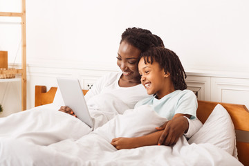 Black mother watching cartoons with her daughter in bed