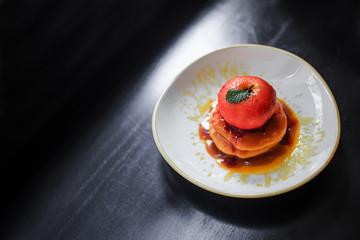 Dessert. Baked apple with red wine, cinnamon and spices and decorated with fresh mint leaf on a plate with pancakes poured with caramel. Light plate on black background.Top view