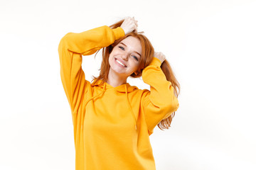 Smiling young redhead woman girl in casual yellow hoodie posing isolated on white wall background studio portrait. People lifestyle concept. Mock up copy space. Having fun holding hair like ponytails.