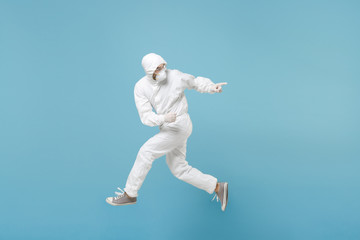 Fototapeta na wymiar Man in white protective suit respirator mask run jump isolated on blue background studio. Epidemic pandemic new rapidly spreading coronavirus 2019-ncov from Wuhan China, medicine flu virus concept.