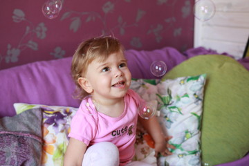 Cute little Caucasian girl one year old plays in her room with soap bubbles, laughs merrily, close-up. Childhood, leisure, games.