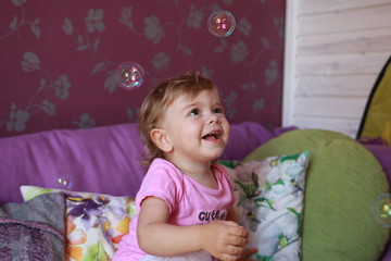 Cute little Caucasian girl one year old plays in her room with soap bubbles, laughs merrily, close-up. Childhood, leisure, games.