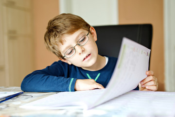 Naklejka premium Hard-working happy school kid boy making homework during quarantine time from corona pandemic disease. Healthy child writing with pen, staying at home. Homeschooling concept