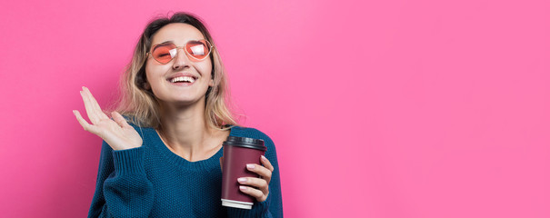 Obraz na płótnie Canvas Glamor woman in glasses in a blue sweater with a drink of coffee on a pink background