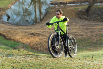 Plakat Cyclist in pants and green jacket on a modern carbon hardtail bike with an air suspension fork. The guy on the top of the hill rides a bike.