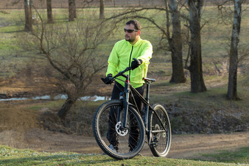 Fototapeta na wymiar Cyclist in pants and green jacket on a modern carbon hardtail bike with an air suspension fork. The guy on the top of the hill rides a bike.