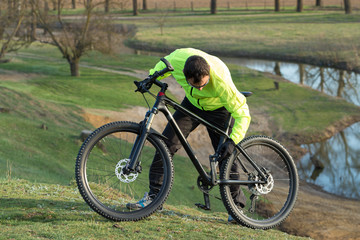 Cyclist in pants and green jacket on a modern carbon hardtail bike with an air suspension fork. The guy on the top of the hill rides a bike.