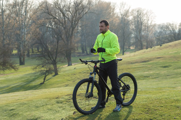 Fototapeta premium Cyclist in pants and green jacket on a modern carbon hardtail bike with an air suspension fork. The guy on the top of the hill rides a bike.