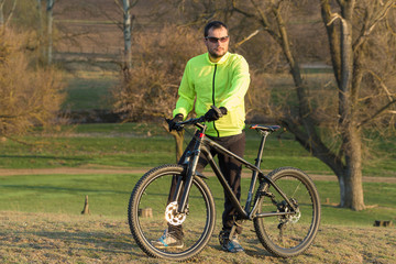 Naklejka premium Cyclist in pants and green jacket on a modern carbon hardtail bike with an air suspension fork. The guy on the top of the hill rides a bike.