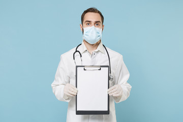 Fototapeta na wymiar Male doctor man in medical gown face mask gloves isolated on blue background. Epidemic pandemic coronavirus 2019-ncov sars covid-19 flu virus concept. Hold clipboard with blank empty sheet workspace.