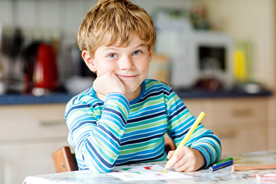 Hard-working happy school kid boy making homework during quarantine time from corona pandemic disease. Healthy child writing with pen, staying at home. Homeschooling concept
