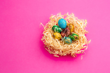 Painted easter eggs lie in a nest of shavings.