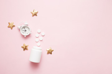 Pills, bottle and white alarm clock with stars on pink pastel background. Concept Insomnia, sleep problems, time to take pills and treatment. Top view, flat lay, copy space.