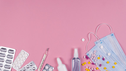 Protective medicine mask, antiseptic thermometer and pills on pink background, flat lay. Concept of doctor table and health care.