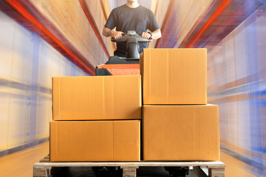 Warehouse worker driving electric forklift pallet jack unloading shipment pallet goods, package boxes, warehouse inventory management and delivery services