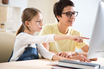 Woman and her little daughter are using a computer and smiling