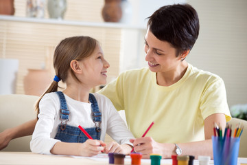 Happy mother and her daughter drawing in a room together