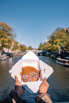 Amsterdam Netherlands, woman hand with Stroopwafel in Amsterdam - typical Dutch food - two circular pieces of waffle filled with caramel-like syrup