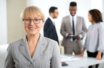 Portrait of happy senior business woman in an office with colleagues on the background