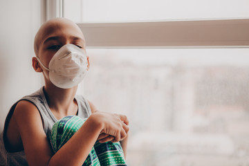 Mask-wearing boy looking outside the window. sick child without hair in the hospital, wears a protective mask and looks out the window. sick boy without hair