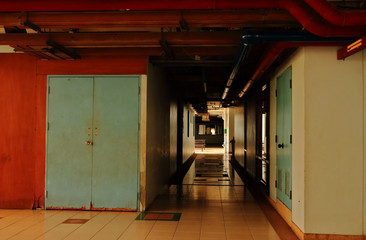 Silent corridor in a building next to decaying blue wooden door, with red water pipes installed on the ceiling
