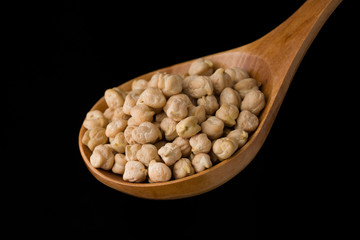 Chickpeas in a wooden spoon on a black background. Close up , macro