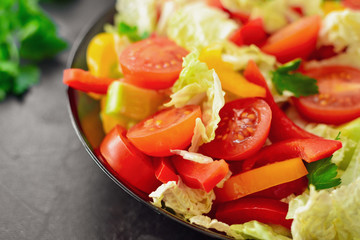 Spring vegetable salad. Salad, tomatoes, cabbage, dressing, bell pepper, cucumber, parsley. Dark background, top view. Close up.