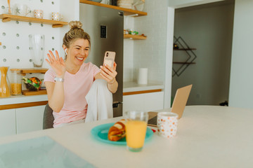 Portrait of young blonde woman having video call with her friends over smartphone. Young woman is having video call in order to keep distance from everybody due to COVID19 pandemic.