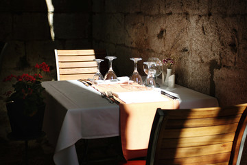 Set empty tables in cozy cafe with empty wine glasses in old european street in summer time without visitors