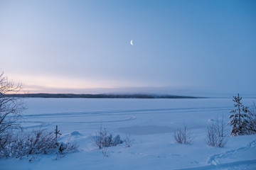 Winter landscape in Russia. New moon rising over forest