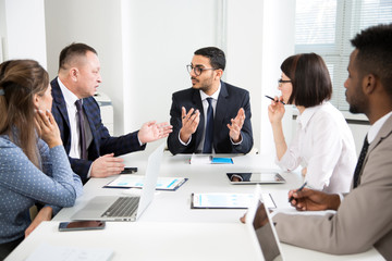 International group of business people working and communicating sitting near office desk.