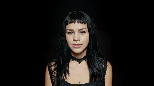 Woman with pierced lips against black background. Young woman in gothic style looking at camera.