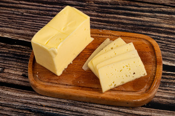 Wooden butter dish with a piece of butter and slices of cheese on a wooden background. Close up.
